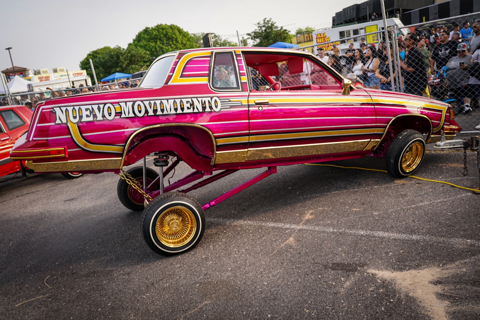 Pink and gold Nuevo Movimiento lowrider on hydraulics at a car show